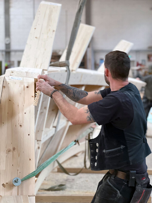 Ein Zimmermann montiert in der Montagehalle ein Bogendachsegment