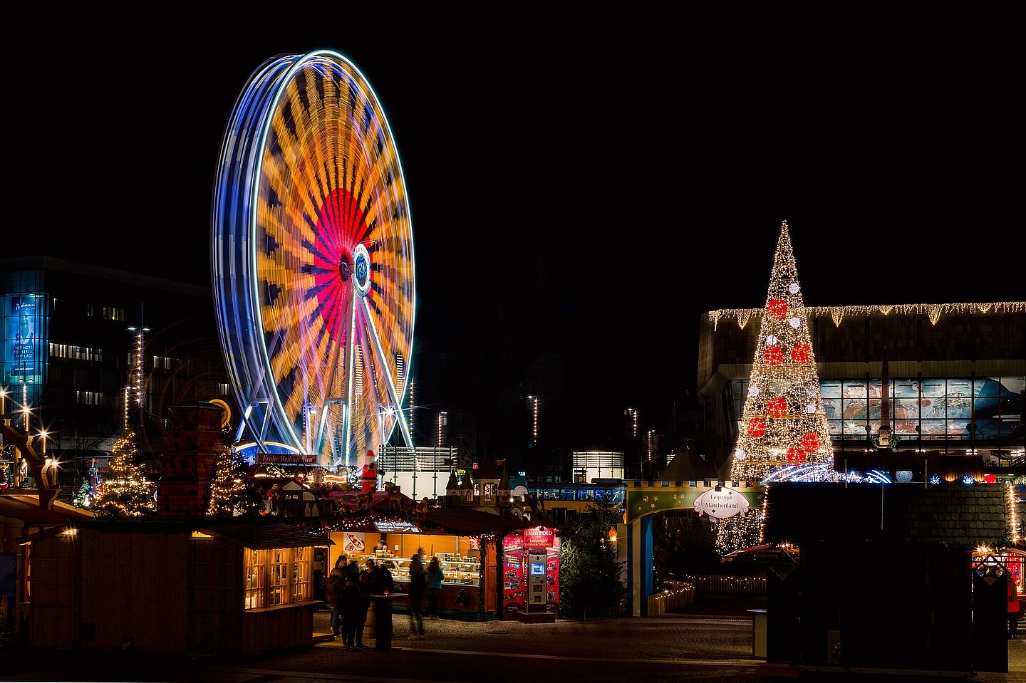 Weihnachtsmarkt in Leipzig (Foto: Pixabay) Nachtaufnahme vom Augustusplatz zu Zeiten des Weihnachtsmarktes, also mit mit erleuchteten Buden und in farbiges Licht getauchtes Riesenrad.