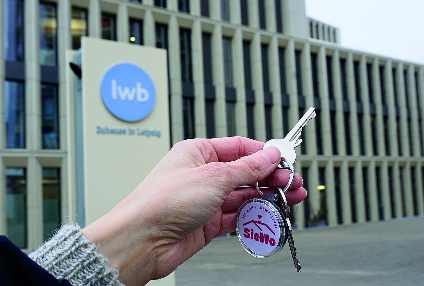 SieWo-Kooperation Hand mit einem Schlüssel vor einem Gebäude der LWB