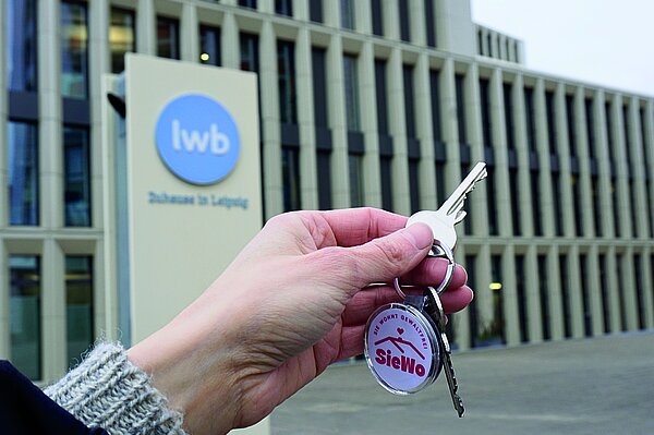 SieWo-Kooperation Hand mit einem Schlüssel vor einem Gebäude der LWB