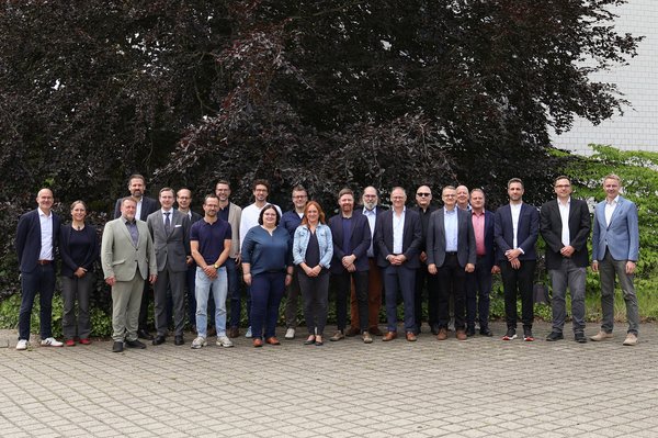 30 Personen stehen im Freien für ein Gruppenbild nebeneinander