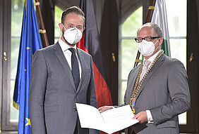Zwei Männer feierlich mit Maske und Urkunde